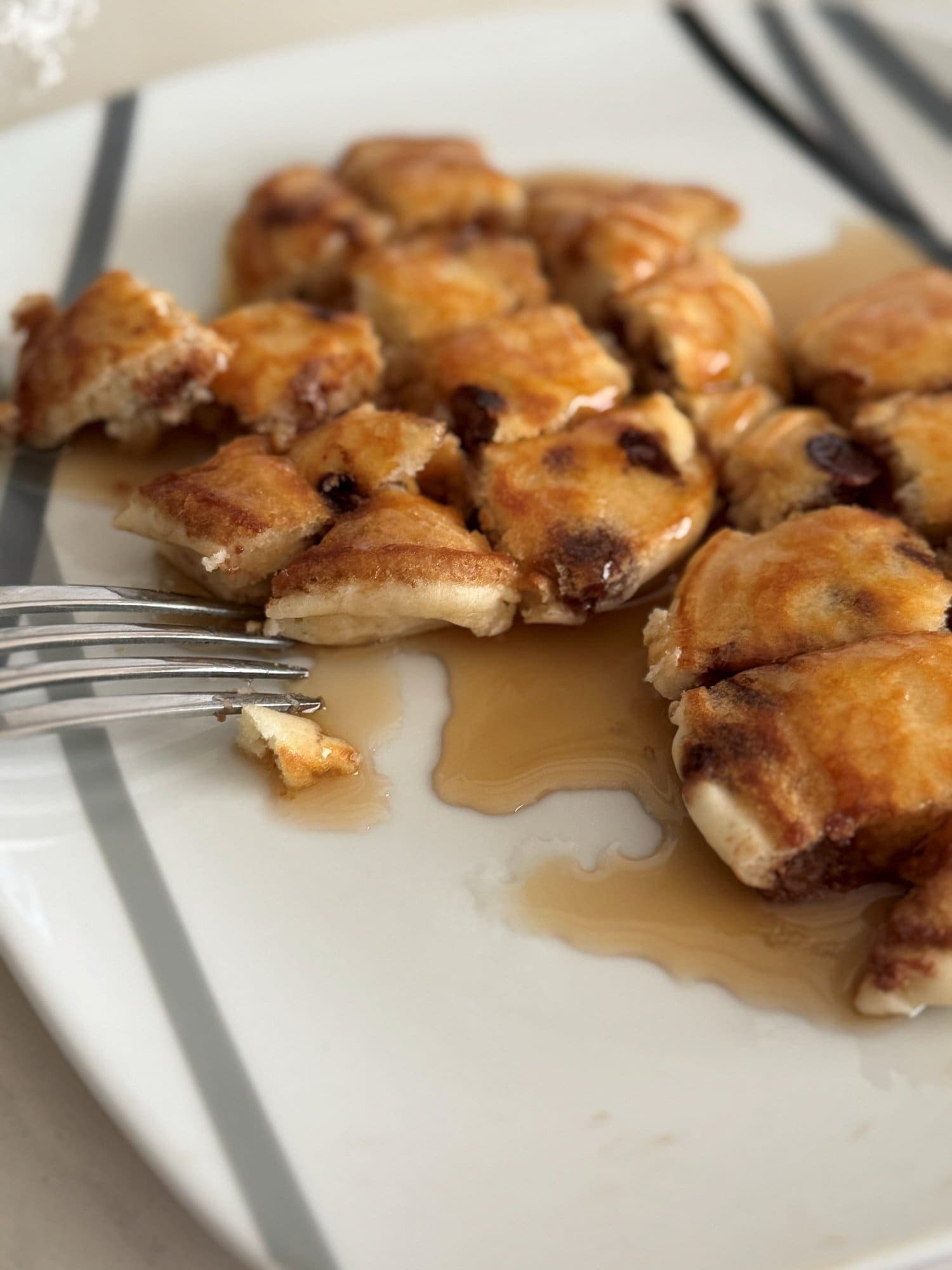 A plate of chocolate chip pancakes cut into bite sized pieces with maple syrup pooled around them