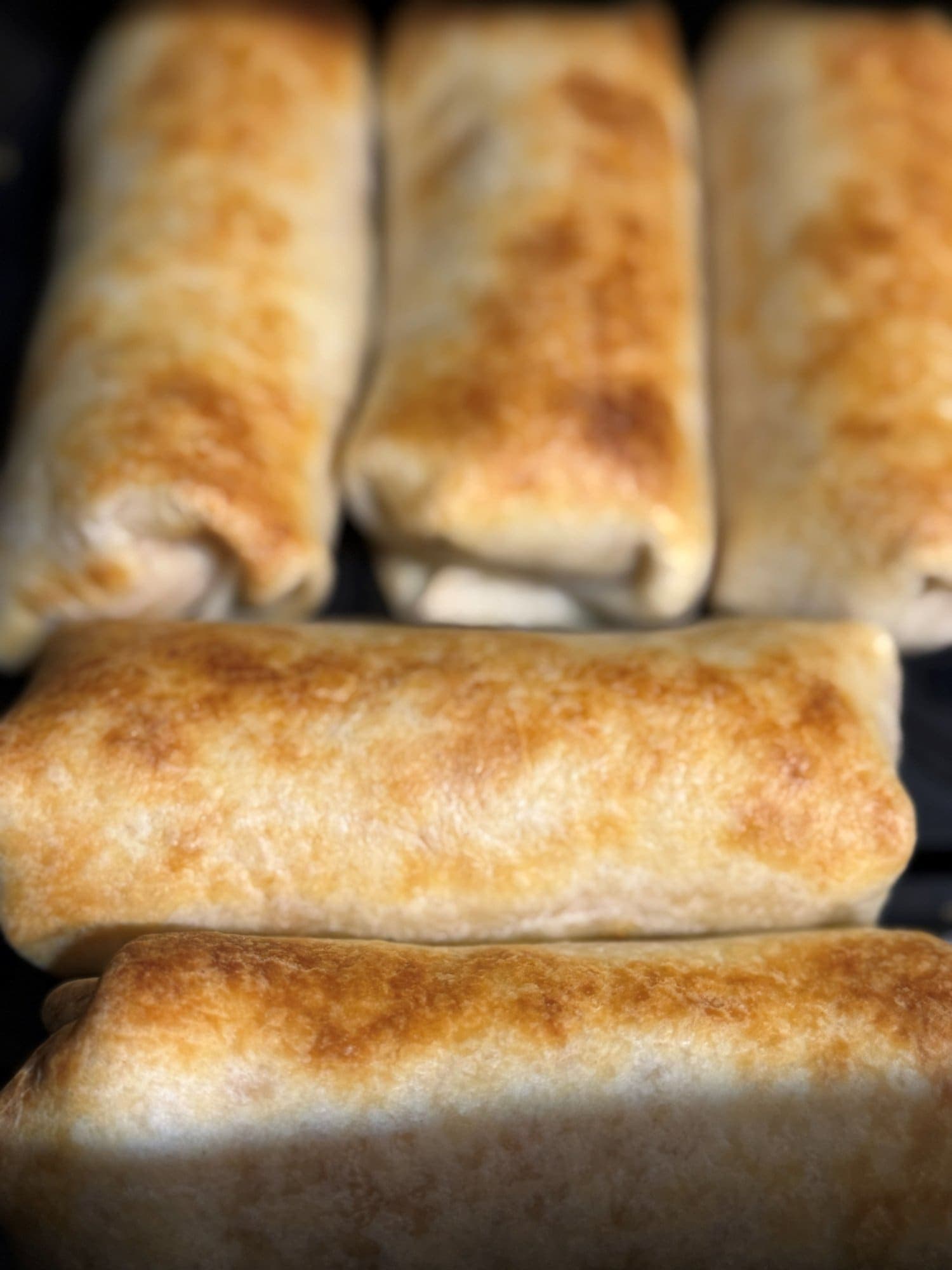 Golden air fried chicken taquitos lined up in an air fryer basket