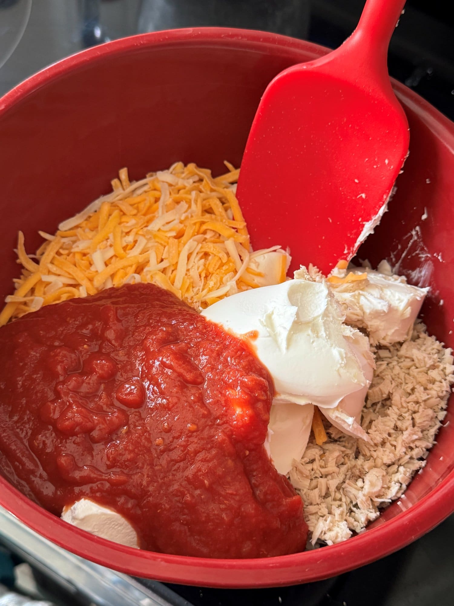 Shredded chicken, grated cheese, cream cheese and tomato sauce in a red mixing bowl
