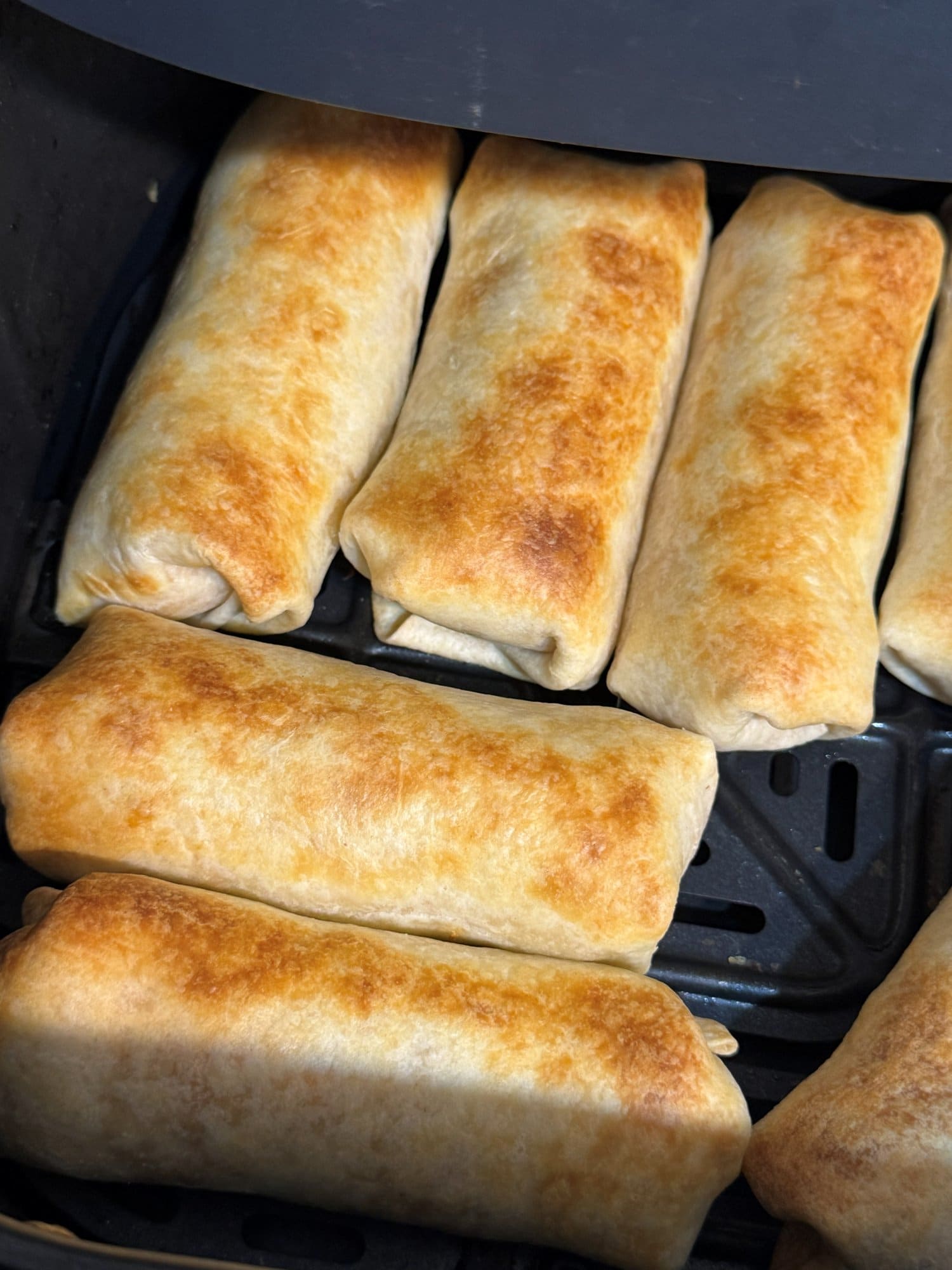 Golden brown taquitos in an air fryer basket after cooking