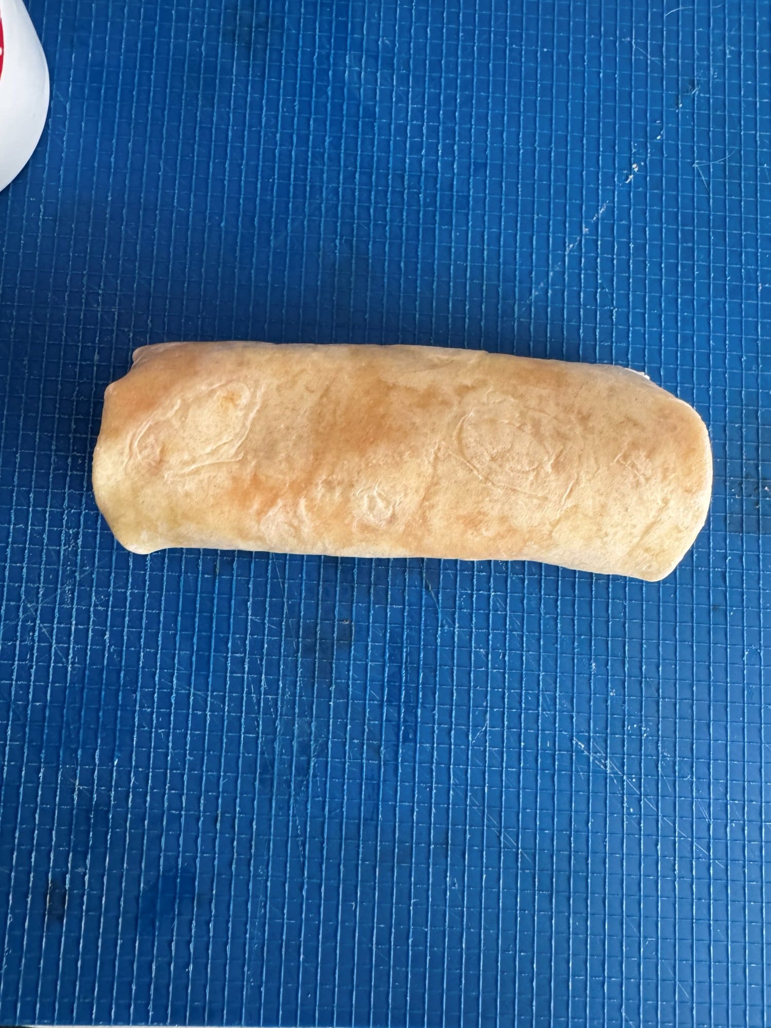 A rolled taquito resting seam side down on a blue cutting board